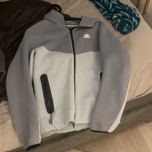 Nike grå och ljusblå vindjacka S - Nike  i snygg tvåfärgad design med grå och ljusblå paneler. Jackan har huva, hel dragkedja framtill och svarta detaljer vid fickorna. Perfekt för dig som vill ha en sportig och clean look. Klassisk Nike-logga på bröstet.  Jag har andvänt 9 gånger 
