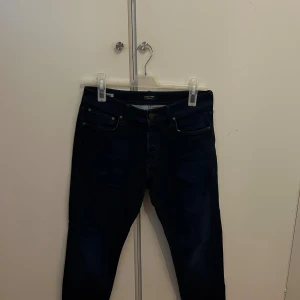 Mörkblå jeans från Jack & Jones - Snygga mörkblå jeans från Jack & Jones med klassisk femficksdesign och smal passform. Jeansen har en stilren look med subtila slitningar och raka ben. Perfekta för dig som gillar en enkel och modern stil.