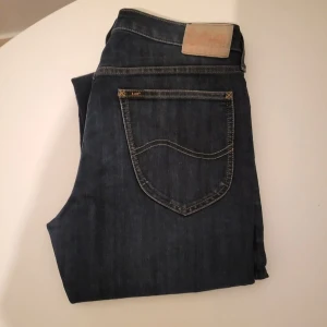 Mörkblå jeans från Lee w31 L32 - Snygga mörkblå jeans från Lee med klassisk femficksdesign och raka ben. Jeansen har kontrastsömmar, Lee-logga på bakfickan och en ljus läderpatch i midjan. Materialet är slitstarkt denim i bomull och passformen är straight för en clean look.