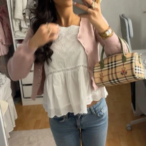 Rosa kofta från Odd Molly - Supersöt rosa kofta från Odd Molly med v-ringad hals och knappar framtill. Koftan är stickad i mjukt material och har långa ärmar. Perfekt att slänga över en topp för en chill och feminin look. Passar dig som gillar pastell och comfy vibes.