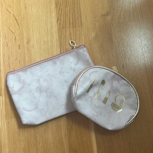 Två ljusrosa necessärer med marmormönster - Säljer två snygga necessärer i ljusrosa med marmormönster och dragkedja. Den ena har guldfärgade sminkdetaljer på framsidan och båda har ljus insida. Perfekt för smink eller småprylar, stilrena och lätta att ta med sig.