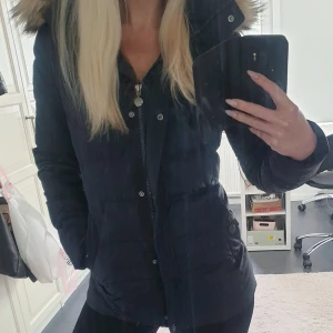 Dunjacka Tommy Hilfiger  - Blåsvart dunjacka från Tommy Hilfiger i jättefint skick.  Avtagbar luva med päls. Insvängd midja och fickor.  Dragkedja och knappar framtill.   Funkar både under höst och vinter.   Storlek XS, passar även S. Använd vid fåtal tillfällen.