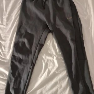 Svarta mjukisbyxor från BOSS - Svarta mjukisbyxor från BOSS med diskret logga på ena benet. Byxorna har dragsko i midjan och ribbade detaljer längs sidorna. Tillverkade i mjukt bomullsmaterial för maximal komfort och en avslappnad look.