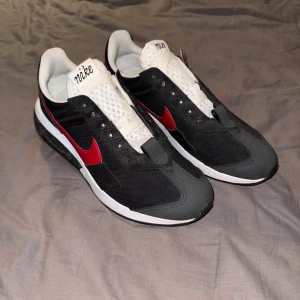 Nike AIR MAX PRE DAY sneakers svart/röd strl 44.5 - Nike Air max Pre Day sneakers i svart och vitt med röda detaljer och klassisk swoosh på sidorna. Ovandel i textil och syntet, vit plös med svart Nike-logga och svart yttersula med bra grepp. Snygg kontrast mellan färgerna och sportig vibe. Perfekt för dig som gillar streetwear. Skorna är använda en gång, och är i ny skick. Priset är ej hugget i sten.