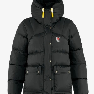 Svart Fjällräven jacka  - Säljer en svart pufferjacka från Fjällräven med gul snörning i huvan och klassisk logga på bröstet. Jackan har stora fickor med knappar, dragkedja och tryckknappar framtill. Perfekt för kalla dagar med sin fluffiga och isolerande design. Den är varm och skön, storlek S. Sparsamt använd. 