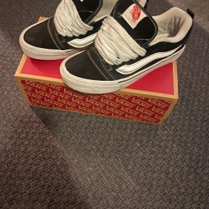 Svarta och vita Vans Knu Skool sneakers - Klassiska Vans Knu Skool sneakers i svart och vitt med den ikoniska vita sidoremsan. Skorna har snörning, vit platt sula och är tillverkade i mocka och canvas. Perfekta för en streetstyle-look och passar till det mesta i garderoben.