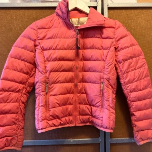 Parajumpers storlek XS (8-10år)  - Säljer en röd pufferjacka med horisontella quiltade sektioner och hög krage. Jackan har två fickor med dragkedja och en hel dragkedja framtill. Materialet är syntet och jackan är långärmad med en croppad passform. Har fler bilder även på Parajumpers lapparna.