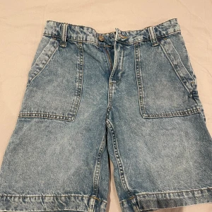 jeansshorts med stora fickor - Säljer ett par jeansshorts i ljusblå denim med stora fram- och bakfickor samt extra sidoficka. Klassisk femficksmodell med bälteshällor och dragkedja. Perfekta för en chill och avslappnad stil i sommar.