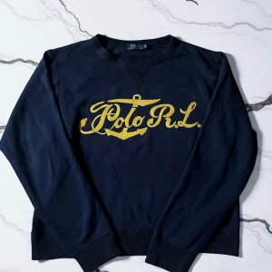Ralph lauren tröja - 🧥 Polo Ralph Lauren sweatshirt 💛 Snygg marinblå tröja med guldfärgat Polo R.L.-tryck och ankardesign framtill! 📏 Storlek: 170 (XL i barnstorlek) ✨ Skick: Väldigt bra – inga hål eller fläckar, bara lätt använt! 🧼 Nyttvättad och redo att användas 👌 💙 Klassisk stil som passar både till vardag och fest!