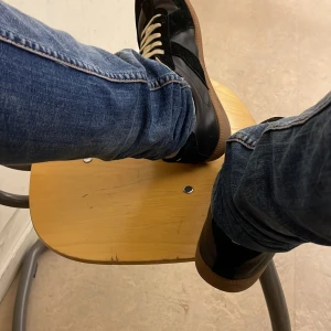 Svarta maison margiela - Säljer ett par svarta sneakers med snygga kontrasterande vita snören och brun gummisula. Skorna har en klassisk och stilren design med rund tå och paneler i olika material, vilket ger en cool och tidlös look. Perfekta för dig som gillar streetstyle.