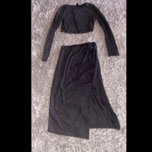 Glittrig svart långklänning från SHEIN - Svart glittrig långklänning från SHEIN i storlek S. Klänningen har långärmad croppad överdel och en lång kjol med slits. Materialet är mjukt och stretchigt med 76% polyamid och 24% polyester. Perfekt för dig som vill sticka ut med lite extra glitter.