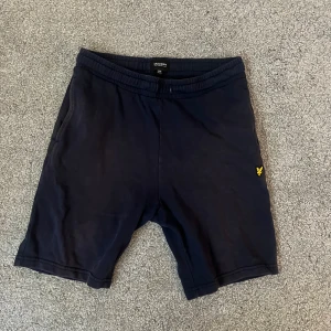 Mörkblå shorts från Lyle & Scott - Mörkblå shorts från Lyle & Scott med elastisk midja och sidofickor. Klassisk gul logga broderad på vänster ben. Mjukt bomullsmaterial och en bakficka. Perfekta för chill dagar eller träning.