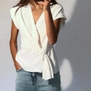 Vit omlottopp med knyt i midjan - Säljer en stilren vit omlottopp med v-ringning och knyt i midjan. 