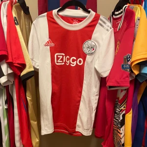 Ajax 2021/22 hemmatröja av Adidas i strl S Äkta Fotbollströja - Ajax hemmatröja från säsongen 2021/22 Adidas i klassiskt röd och vit design med Ziggo sponsortryck. Tröjan är i mycket bra skick och i storlek S, Äkta
