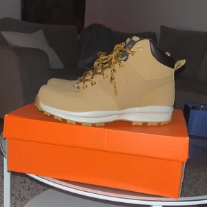 Nike boots - Säljer ett par snygga beige boots från Nike med robust snörning och grov sula. Skorna har detaljer i mörkbrunt vid ankeln och guldiga öljetter. Perfekta för höst och vinter, med slitstark ovandel och bekväm passform. Klassisk Nike-logga på sidan.
