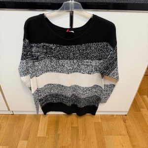 Svart och vit randig stickad tröja - Snygg stickad tröja med breda ränder i svart, grått och vitt. Tröjan har rund hals och långärmade ärmar. Den har en loose passform och är superenkel att matcha med jeans eller leggings.