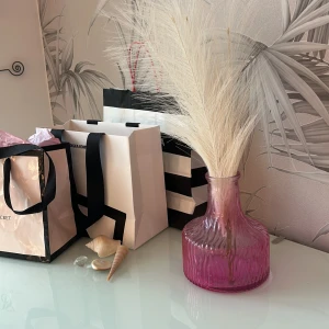 Jag säljer en fin rosa glasvas. - Bilderna visar en dekorativ rosa glasvas med vågig struktur. Vasen är i fint skick utan synliga sprickor eller skador och passar perfekt som inredningsdetalj för blommor eller pampasgräs. Den har en bred botten och smal hals, vilket ger ett modernt och stilrent uttryck.