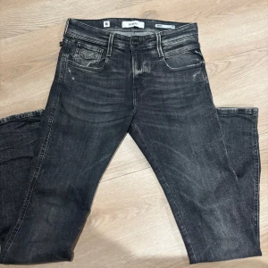 Replay Anbass svarta jeans - Säljer ett par Replay Anbass jeans i svart tvätt med snyggt slitna detaljer. Klassisk femficksmodell med smal passform och normal midja. Jeansen har Replay-logga på fickan och bak på linningen. Perfekta för dig som gillar en modern och stilren look. L - 32