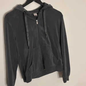 Mörkgrå hoodie i velour från Gina Tricot - Mjuk och stilren mörkgrå hoodie i velour från Gina Tricot. Tröjan har dragkedja framtill, huva med snörning och två fickor. En av metallsluten på snörena saknas därav priset💗