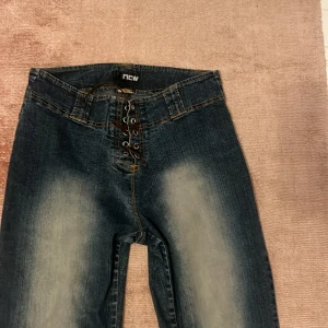  jeans med snörning  - Snygga blå jeans med bootcut passform från Now. Byxorna har cool snörning framtill istället för klassisk dragkedja, slitna detaljer vid benslut och ljusare tvättade partier på benen. I storlek 40 men jag skulle säga att dom är 36-38