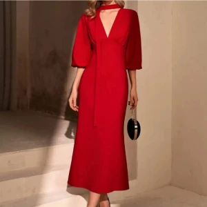 Röd långklänning med puffärm och v-ringning - Snygg röd långklänning med djup v-ringning, puffiga trekvartsärmar och knytband i halsen. Klänningen har en elegant siluett och dragkedja i ryggen. Perfekt för dig som vill sticka ut med en klassisk men trendig look.