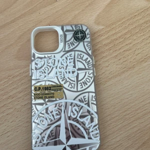 Stone Island iPhone Skal - Unikt Stone Island-skal för iPhone med ikonisk logotyp och detaljerad design. Skalet är i ny skick Ger din telefon ett exklusivt och trendigt utseende samtidigt som den skyddas mot stötar och repor. Passar till iPhone 13 14 och även till iPhone 15 