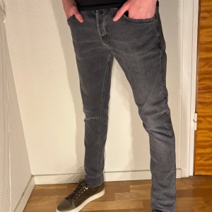 Dondup jeans George  - Säljer ett par grå jeans med svarta detaljer på bakfickorna. Jeansen har en slim passform och klassisk femficksdesign. De är tillverkade i stretchigt jeanstyg för extra komfort och har normal midja. Perfekta för dig som gillar en stilren och modern look. (Storlek 33, sitter som 31-32)