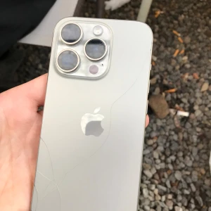 iPhone 15 Pro  - Snygg iPhone 15 pro titan färg.trippelkamera och stor skärm. Baksidan har en tydlig spricka men kamerorna och skärmen ser ut att vara i gott skick. Perfekt för dig som vill ha en kraftfull mobil till ett bra pris trots kosmetiskt slitage.