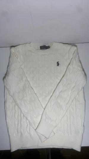 Vit kabelstickad tröja Polo Ralph Lauren - Kabelstickad vit tröja från Polo Ralph Lauren med klassisk rund hals och broderad logga på bröstet. Skriv gärna om du vill diskutera om priset!