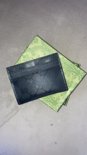 Svart kortfodral  - Snyggt svart kortfodral från med diskret mönster av små rosetter över hela ytan. Tillverkat i exklusivt skinn med en stilren och modern look. Perfekt för att hålla dina kort organiserade och ser riktigt lyxigt ut i fickan.