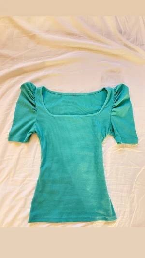 Turkos T-shirt - Hej! Säljer denna ursöta u-ringade turkosa t-shirten med en tajt passform nedtill och lite puffigare axlar upptill. T-shirten har endast blivit använd 2-3 ggr så den är därav i mycket fint skick utan några defekter. Perfekt topp om du vill se brun och fräsch ut!🩵 Om du skulle fundera över något är det bara att höra av dig.