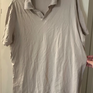 Beige kortärmad pikétröja Dressmann 3XL - Beige kortärmad pikétröja från Dressmann i storlek 3XL. Pikétröjan  är tillverkad av 100% Supima bomull och har en klassisk krage utan knappar framtill. Perfekt för en avslappnad och stilren look.