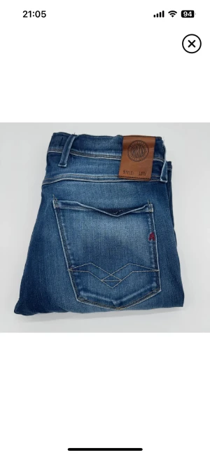 Replay Anbass blå jeans med slitningar - Snygga Replay Anbass jeans i blå tvätt med slitningar och lätt distressed look. Klassisk femficksmodell, läderpatch bak i midjan och raka ben. Jeansen har slim passform och är tillverkade i stretchigt denim för skön känsla.