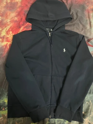  Polo Ralph Lauren hoodie - Snygg marinblå hoodie från Polo Ralph Lauren med klassisk vit broderad logga på bröstet. Tröjan har huva, dragkedja framtill och långa ärmar. Tillverkad i mjuk bomull som är skön att ha på sig. Självklart tvättas den innan den fraktas. Skriv gärna om du vill diskutera priset!