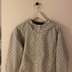 Jacka - Säljer en snygg jacka, med mönster i grått och vitt. Jackan har huva med snörning, dragkedja framtill.. Perfekt för dig som gillar streetwear och vill sticka ut med designerplagg. Det går även att vända jackan ur och in så jackan blir brun. 