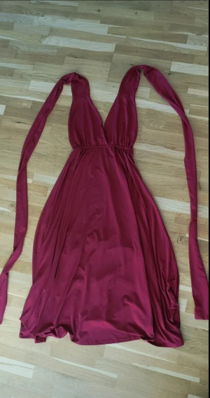 Vinröd infinityklänning - Vinröd infinityklänning i mjukt tyg. Klänningen kan stylas på massor av olika sätt med de långa banden – axelbandslös, omlott, halterneck eller offshoulder. Perfekt för dig som vill ha en unik look varje gång!
