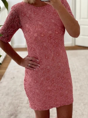 Spetsklänning från Saint Tropez - Supersöt kort rosa klänning från Saint Tropez i storlek XS. Klänningen har blommigt spetsmönster, rund halsringning och halvärmade ärmar. Den är figurnära och har dragkedja i ryggen. Perfekt för dig som vill sticka ut med en feminin och trendig look.