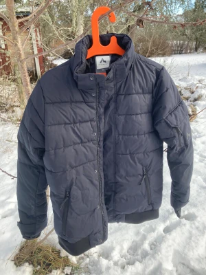 Svart pufferjacka från McKinley - Svart pufferjacka från McKinley med hög krage och dragkedja framtill. Jackan har två snedställda fickor med dragkedja och ribbade muddar vid ärmslut och nederkant. Perfekt för kalla dagar och riktigt skön att bära.