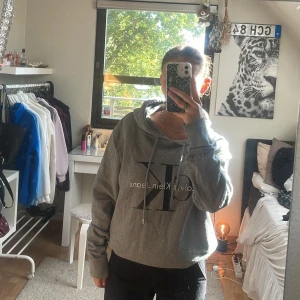 Grå hoodie från Calvin Klein Jeans - Säljer en grå hoodie från Calvin Klein Jeans med stor CK-logga framtill. Tröjan har huva med snörning, långa ärmar och en relaxed passform. ❤️❤️
