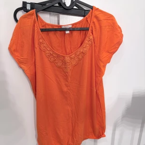 Orange blus med spets från Esprit - Orange blus från Esprit med korta ärmar och rund halsringning dekorerad med snygg spetsdetalj framtill. Tillverkad i mjuk bomull, perfekt för dig som gillar färg och vill ha en luftig och bekväm topp med lite extra detalj.