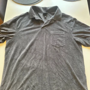 Grå ribbad skjorta från H&M - Säljer en grå ribbad skjorta från H&M i relaxed fit. Skjortan har klassisk krage, korta ärmar och en bröstficka. Materialet är mjukt och har en tydlig ribbad struktur som ger en cool vibe. Perfekt för dig som gillar enkel och stilren design.