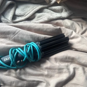 Lyko Triple Barrel Hair Waver - Lyko Triple Barrel Hair Waver med svart design och turkos sladd. Skapar snygga vågor i håret, har on/off-knapp och justerbar värme. Produkten ser välvårdad ut utan synligt slitage eller defekter. Perfekt för styling hemma eller på resan. Aldrig använt 