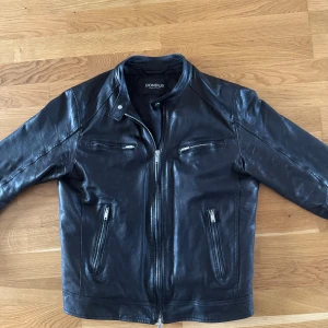 Svart skinnjacka från Dondup - Snygg svart skinnjacka från Dondup med klassisk krage och flera dragkedjeförsedda fickor. Jackan har en stilren look med raka linjer och silverfärgade detaljer. Perfekt för dig som vill ha en grym och tidlös jacka med edge. Nypris 11000kr självklart äkta! Storlek Small/medium