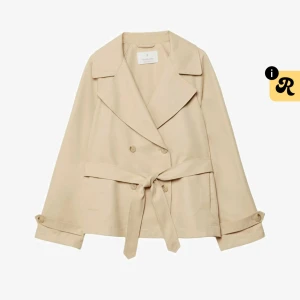 Beige trenchcoat med bälte  - Snygg beige trenchcoat  med klassisk krage, dubbelknäppning och bälte i midjan. Jackan har långa ärmar med knappdetalj vid mudden och en stilren, loose passform. Perfekt för dig som gillar minimalistisk och clean stil.
