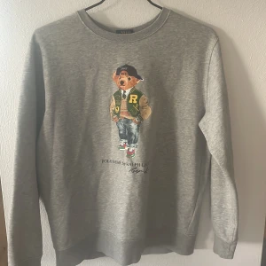 Grå sweatshirt Polo Bear Ralph Lauren - Säljer en grå sweatshirt från Polo Ralph Lauren med ikoniskt Polo Bear-tryck framtill. Tröjan har rund hals, långa ärmar och ribbade muddar. Perfekt för dig som gillar streetstyle och klassiska märken. Tröjan är i bra skick och sparsamt använd, pris kan diskuteras!