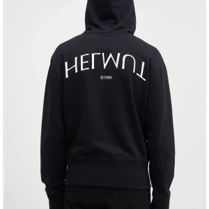 Svart hoodie från Helmut Lang, L - Svart hoodie från Helmut Lang med liten logga på bröstet och stor logga på ryggen. Klassisk känguruficka, huva med metallöljetter och ribbade muddar. Tillverkad i mjuk bomull för en skön känsla. 