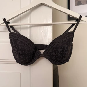 Svart/väldigt mörkblå/gråaktig blommig bh från H&M - Bh från H&M med vadderade kupor (ingen push up) och justerbara axelband. Sidorna har ett diskret blommigt mönster i spets och kuporna är släta med dekorativ kant. Perfekt för dig som gillar en klassisk look med en twist.
