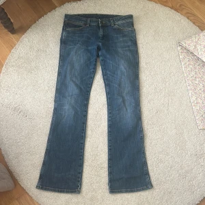 Blå bootcut jeans från Wrangler W30 L32 - Snygga blå jeans från Wrangler med klassisk bootcut-passform och raka ben. Jeansen har fem fickor, kontrastsömmar och ikoniska W-broderade bakfickor. Tillverkade i slitstarkt denim med en cool tvättad look. Perfekta för dig som gillar retrovibbar och avslappnad stil.