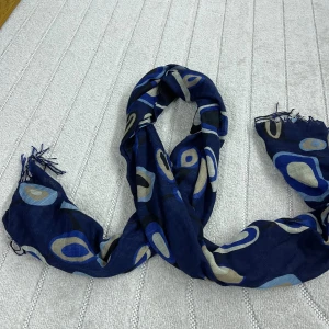 Blå halsduk med ovalt mönster från Vero Moda - Snygg halsduk i marinblått med ovala mönster i beige, svart och olika blå nyanser. Tunt och mjukt material med fransar i ändarna, perfekt att slänga över axlarna för en cool look. Lätt att matcha med jacka eller tröja.
