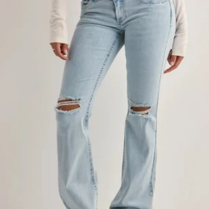 Ljusblå jeans med slitna knän - Snygga ljusblå jeans med bootcut  och slitna hål vid knäna. Baktill finns coola fickor med rosa zigzag-broderi som ger extra attityd. Jeansen har klassisk femficksdesign och är tillverkade i mjukt denimtyg.